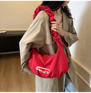 Détail du sac bandoulière rouge en toile avec plis en demi-lune et logo blanc