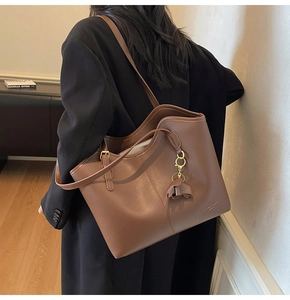 Detailed macro view of a brown leather tote bag with elegant gold branding and side tassel