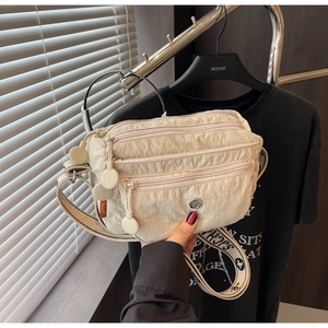 Detail of beige nylon crossbody bag with three zipper pockets and woven letter strap