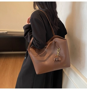 Detail of a brown leather tote bag with elegant bow pendant and gold lettering