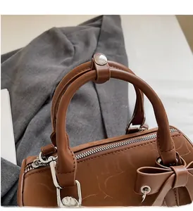 Detailed close-up of brown textured leather cylinder bag with silver metal zipper and bow