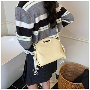 Detail view of pale yellow leather tote bag with white tassels and cutout handle design