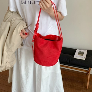 Detail of red matte suede bucket bag featuring scalloped edges and slim shoulder straps