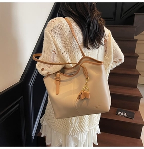 Cream tote bag with brown trim and bow charm shown on model in a stylish setting