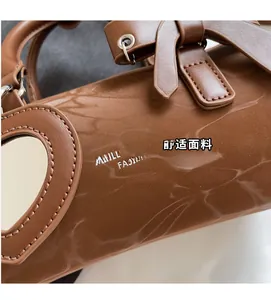 Detail of a brown leather cylinder bag featuring a heart-shaped mirror pendant