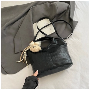 Detail of black crocodile-embossed handbag with cute plush bear charm and woven cord decor