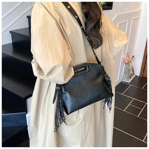 Detail of black leather tote bag featuring long decorative fringes and an adjustable strap