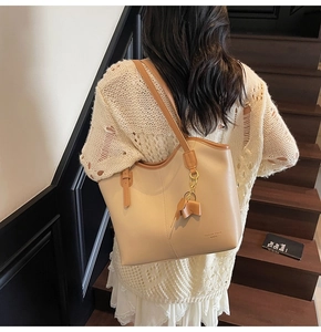 Detail of large beige tote bag with brown contrast straps and a removable bow charm