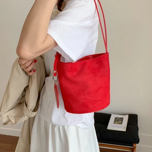 Detail view of red suede bucket bag showing the soft matte texture and leather round pendant