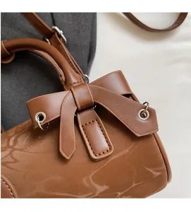 Detail of a brown patent leather cylinder bag with bow and LETAO branding