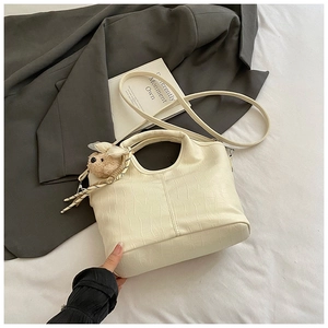 Close-up of cream crocodile pattern handbag with a cute plush bear charm accessory