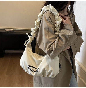 Détail de la bandoulière plissée et étiquette sur le sac croissant en toile beige