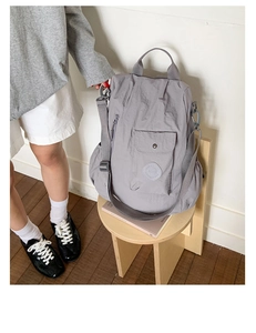 Detailed view of a grey nylon backpack with front flap pocket on a wooden stool