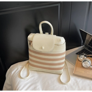 Detail of cream straw backpack with brown stripes and leather top handle on a bed