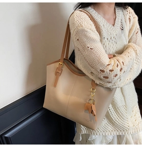 Detail of a large beige tote bag with brown straps and golden hardware on a model