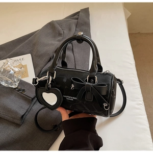 Detail of black nylon cylinder bag featuring a bow and heart-shaped mirror charm