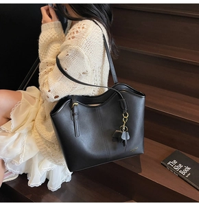 Detail of black leather tote bag with gold logo and leaf charm on wooden stairs