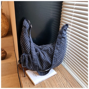 Detail of grid canvas hobo bag with adjustable strap and drawstring bow on wood