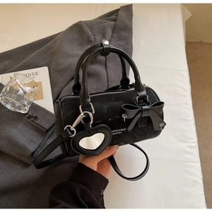 Detail of black cylindrical Boston bag with bow accent and heart mirror on white bedding