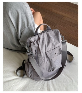 Detail of grey crinkled nylon bag featuring functional side zipper and brand logo patch