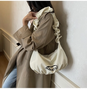 Détail du sac demi-lune en toile beige avec bandoulière plissée et logo imprimé