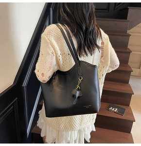 Detail of black tote bag with elephant charm and shoulder straps on wooden stairs