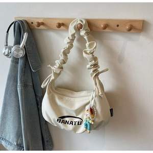 Détail du sac dumpling en toile crème avec bandoulière froncée et pendentif poupée mignon