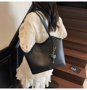 Detail of a black leather tote bag featuring a cute elephant charm on a wooden staircase