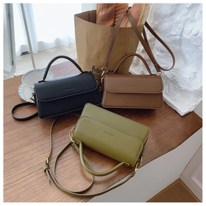 Close-up of minimalist leather flap handbags in black, brown and green on a wooden table