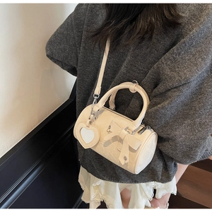 Close-up of cream cylinder bag with bow decoration and heart mirror charm on model