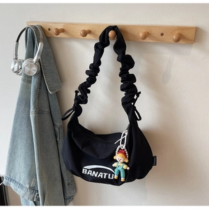 Détail du sac hobo en toile noire avec bandoulière plissée et pendentif poupée mignon