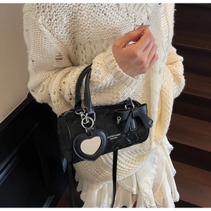 Detail of black cylindrical handbag with bow decoration and heart-shaped mirror charm