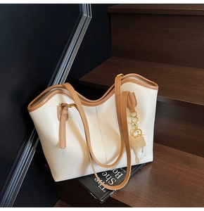 Detail of cream large tote bag with brown trim and cute elephant charm on wooden stairs