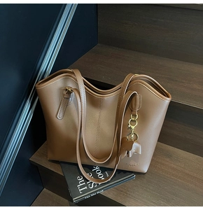 Detail view of brown vintage tote bag with elephant charm on dark wood background