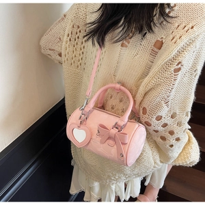 Detail view of pink cylinder bag with bow decoration and heart mirror pendant accessory