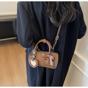 Detail of a brown cylindrical crossbody bag with a bow and heart-shaped mirror pendant