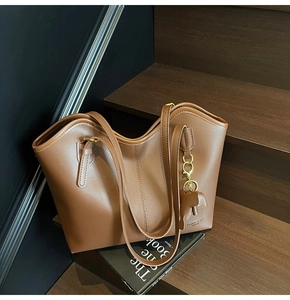 Close-up of caramel brown leather tote bag with elephant charm on wooden steps