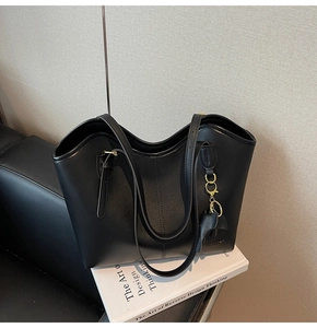 Close-up of black leather tote bag with elephant charm and gold chain detail on art book