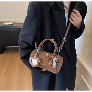 Detail of a brown glossy barrel bag featuring a stylish bow and heart mirror charm