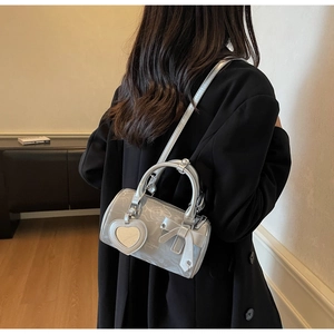 Detail of silver cylinder bag with heart mirror charm and bow accessory on shoulder strap