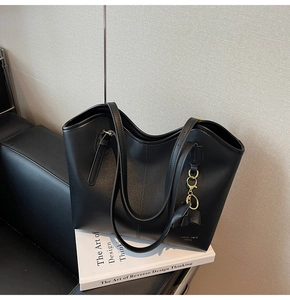 Close-up of black tote bag featuring matte leather texture and gold leaf pendant charm