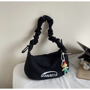 Détail de la bandoulière plissée noire sur sac en toile avec breloque de poupée