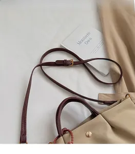 Détail du sac beige en toile avec bandoulière en cuir marron foncé et boucles en métal doré