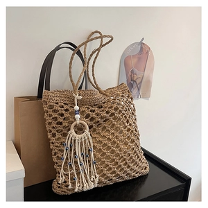 Detail of hand-woven straw tote bag featuring bohemian tassel with evil eye charms
