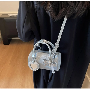 Silver metallic cylinder bag with bow detail and heart charm shown on model's shoulder