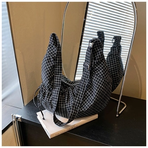 Detail of checkered pattern crescent hobo bag resting on a black podium with soft window light