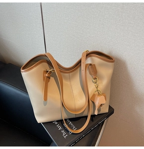 Detail shot of a large beige tote bag with brown trim and elephant charm on a sofa