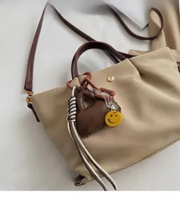Détail du sac bandoulière en nylon beige avec poignées en cuir marron et breloques