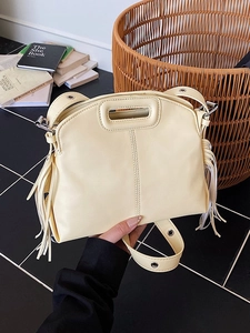 Cream leather tote bag with unique cutout handle and long tassels, shown in a lifestyle setting