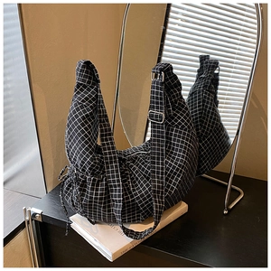 Detail view of checkerboard crescent bag resting on a book with stylish strap buckle